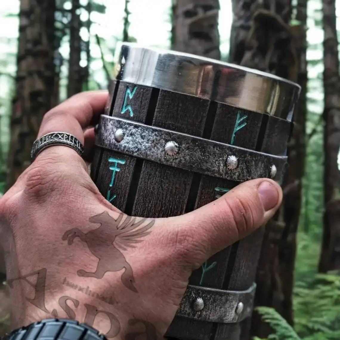 Viking symbolism, runes mug held in a forest with rune engravings on a stainless steel barrel-style design.